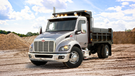 Peterbilt Model 548 Medium Duty Silver Truck with Black Dump Body in Mounded Dirt Field - Thumbnail